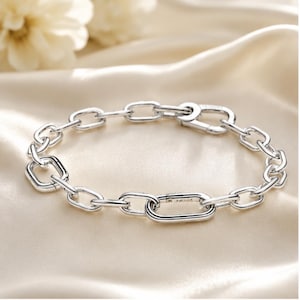 May include: A silver-toned chain link bracelet featuring a series of interconnected oval and rectangular links. The bracelet includes a secure lobster claw clasp mechanism, showcasing a polished metallic finish throughout the entire piece.