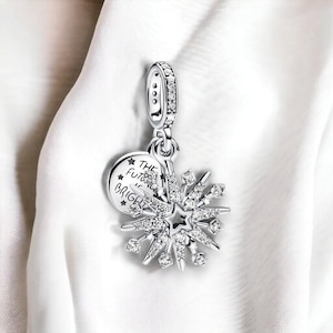 Puede incluir: Un charm de plata con un diseño de estrella estrellada y un charm redondo que dice "El futuro es brillante".