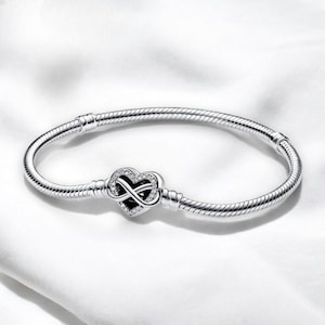 Könnte beinhalten: Ein silbernes Armband mit einem Unendlichkeits-Anhänger in Herzform. Der Anhänger ist mit klaren Zirkonia-Steinen besetzt.