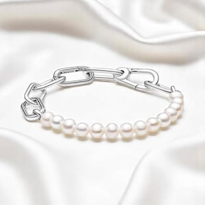 Puede incluir: Un brazalete de cadena de plata con una fila de perlas blancas. La cadena está hecha de eslabones ovalados e interconectados en forma de gancho.