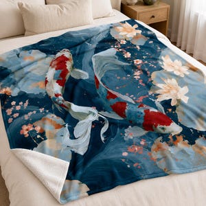 May include: A plush throw blanket featuring a deep blue background with a swirling water pattern. Two koi fish with white and red scales swim across the surface, surrounded by light pink cherry blossoms and white lotus flowers in a soft style.