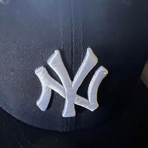 Puede incluir: Gorra de béisbol negra con un logotipo blanco bordado de los New York Yankees.