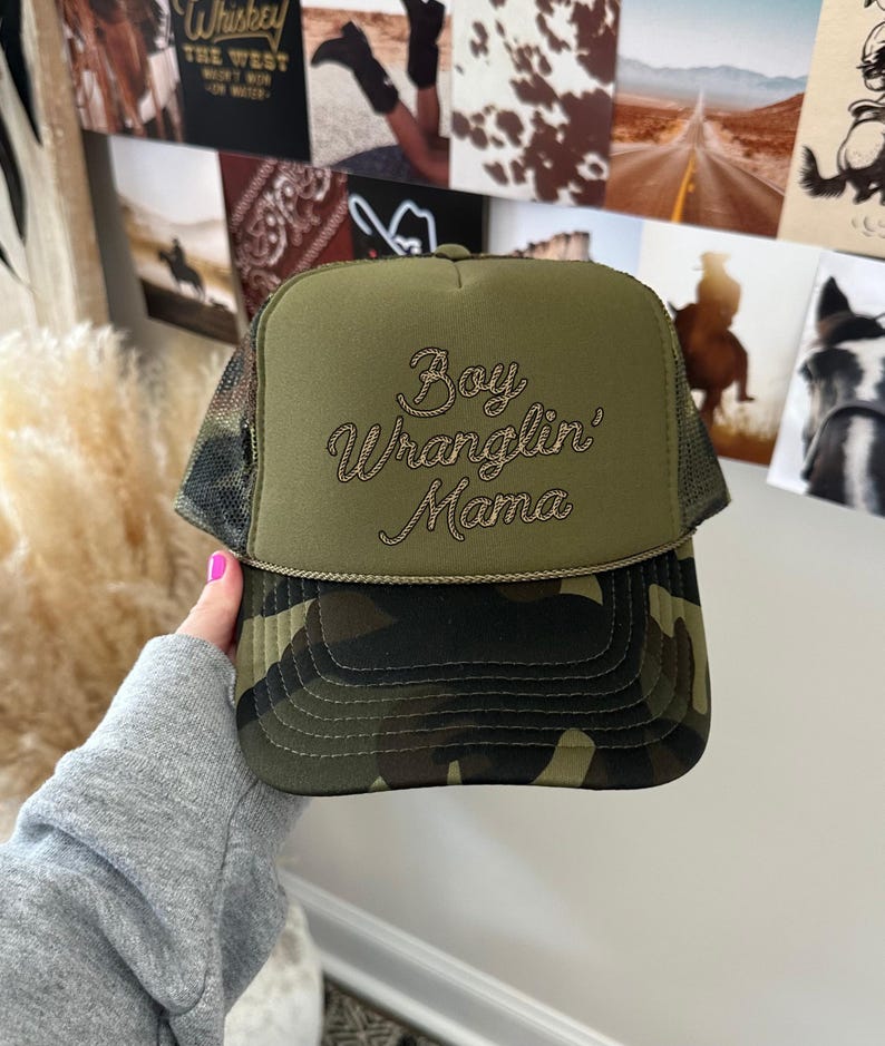 May include: A green camouflage trucker hat with a brown embroidered design that says "Boy Wranglin' Mama".