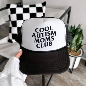 May include: A black and white trucker hat with the text "COOL AUTISM MOMS CLUB" in black lettering on the front.