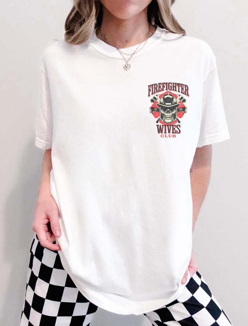 May include: White t-shirt featuring a graphic with the text "Firefighter Wives Club". The graphic includes a skull wearing a firefighter helmet, crossed axes, and the words "Firefighter" and "Wives Club" in red and black.