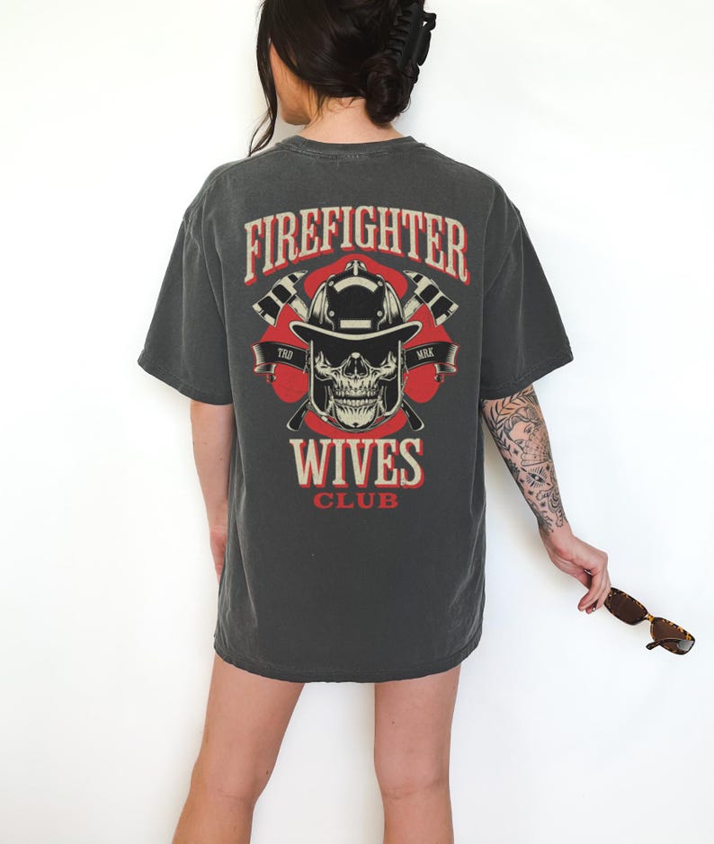 May include: Dark gray t-shirt with a graphic on the back featuring a firefighter's helmet, skull, and crossed axes, with the words "Firefighter Wives Club" in red and white.