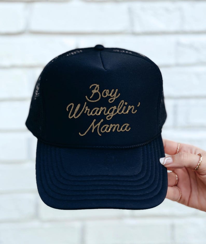 May include: Black trucker hat with a gold embroidered design that says "Boy Wranglin' Mama".