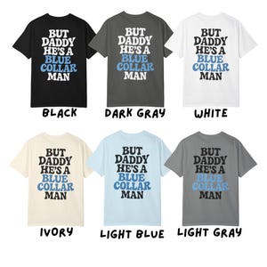 May include: Six t-shirts in various colors: black, dark gray, white, ivory, light blue, and light gray. Each shirt features the text "BUT DADDY HE'S A BLUE COLLAR MAN" in white and blue lettering.