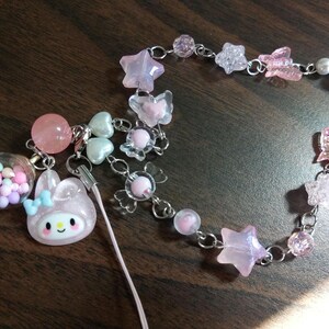 May include: A pink and white charm bracelet with a variety of charms, including stars, butterflies, and a small pink bunny. The bracelet is made of silver chain and has a pink and white string attached to it.