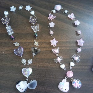 May include: Two pink and white beaded necklaces with charms. One necklace has a pink bunny charm and a clear charm filled with colorful beads. The other necklace has a white dog charm and a clear heart charm.