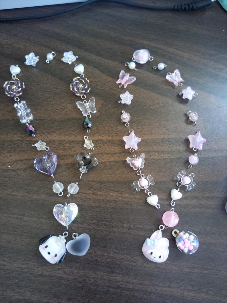 May include: Two pink and white beaded necklaces with charms. One necklace has a pink bunny charm and a clear charm filled with colorful beads. The other necklace has a white dog charm and a clear heart charm.