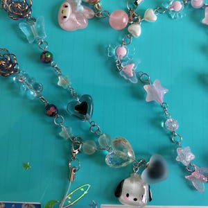 May include: A silver chain with various charms, including hearts, stars, and a cartoon dog. The charms are made of clear, iridescent, and opaque plastic. The chain is strung with clear beads and iridescent beads.