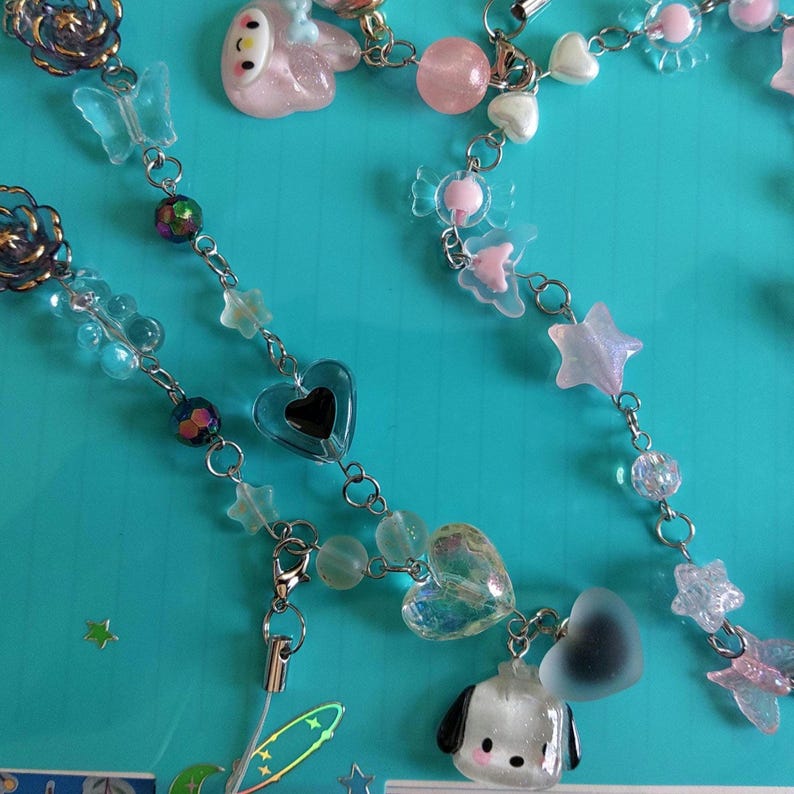 May include: A silver chain with various charms, including hearts, stars, and a cartoon dog. The charms are made of clear, iridescent, and opaque plastic. The chain is strung with clear beads and iridescent beads.