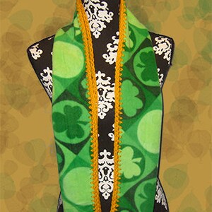 May include: A green and gold scarf with a shamrock pattern. The scarf is crocheted with a gold trim.