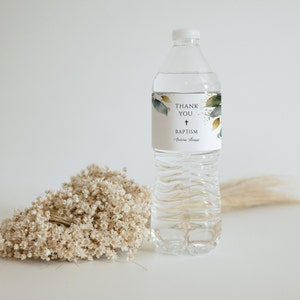 Puede incluir: Una botella de agua de plástico transparente con una etiqueta blanca que dice "Gracias + Bautismo" con una cruz y el nombre "Antonia Grace". La etiqueta tiene un diseño de acuarela de hojas verdes y doradas.