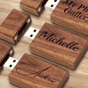 May include: A collection of wooden USB flash drives with a natural wood grain. Each drive features a white USB connector and is engraved with a name or phrase, including "Michelle", "Andrew", and "My Photo Gallery".