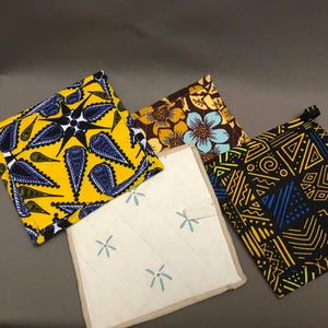 May include: A selection of square pot holders in vibrant patterns. Designs include yellow with blue leaf shapes, brown with floral, cream with blue floral, and black with geometric shapes. Each has a hanging loop.