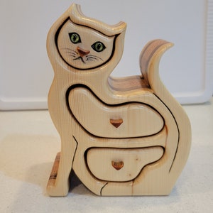 May include: A wooden cat-shaped box with three drawers. The cat has green eyes and a brown nose. The drawers have copper-colored handles.