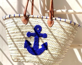 May include: A white woven tote bag with blue trim and a blue anchor design. The bag has brown leather handles.
