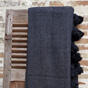 Peut inclure: Une couverture noire avec des pompons noirs le long du bord. La couverture est drapé sur un volet en bois.