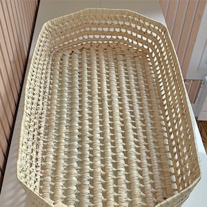 May include: A woven basket made from natural materials, with a rectangular shape and a light beige colour. The basket is made of a tightly woven pattern, creating a sturdy and durable design.