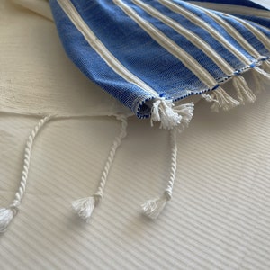 Puede incluir: Un chal de oraci&oacute;n a rayas azules y blancas con borlas blancas. El chal est&aacute; doblado y sobre una superficie blanca.