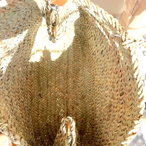 May include: A woven straw tote bag with a brown leather handle and a metal clasp. The bag is empty and the inside is visible.