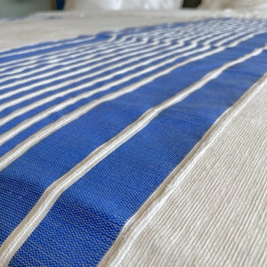 Puede incluir: Un cubrecama blanco con rayas azules y blancas. El cubrecama est&aacute; hecho de una tela suave y texturizada.