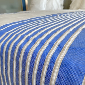 Puede incluir: Primer plano de una colcha a rayas azules y blancas. La colcha est&aacute; hecha de una tela suave y texturizada con un brillo sutil.