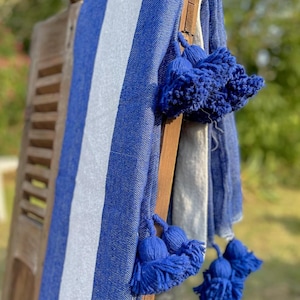 May include: A blue and white striped throw blanket with blue pom-poms on the edges.