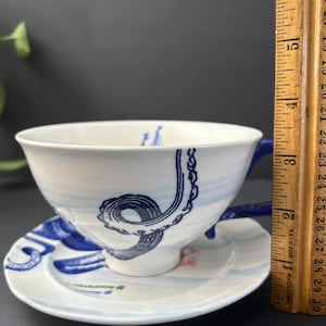 May include: A white ceramic mug with a black handle and the text "But First, Coffee" in a bold, black font. The mug is set against a neutral background, highlighting its simple design.