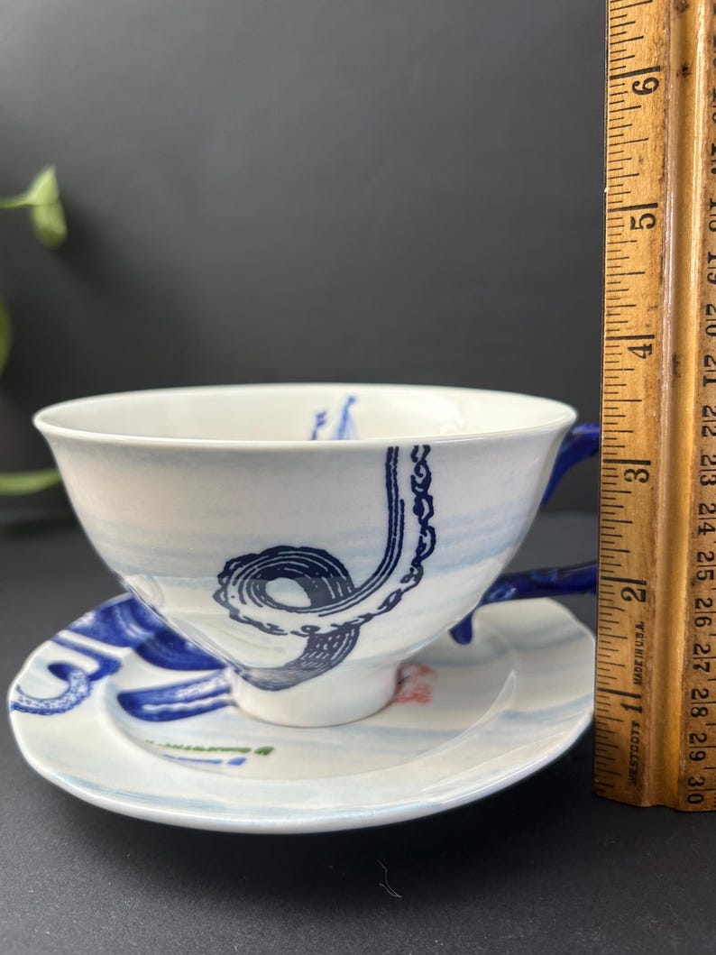 May include: A white ceramic mug with a black handle and the text "But First, Coffee" in a bold, black font. The mug is set against a neutral background, highlighting its simple design.