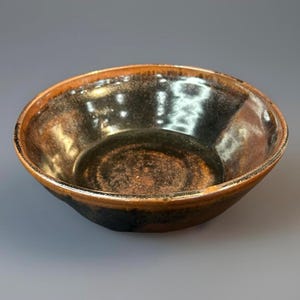 Peut inclure: Un bol en céramique fait à la main avec un intérieur marron foncé et un bord marron clair. Le bol a une surface tachetée et texturée et une finition brillante. L'extérieur est de couleur marron foncé. Ce bol est adapté pour servir des aliments.