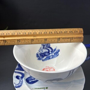 May include: White teacup and saucer set with blue nautical illustrations. The teacup is approximately 4 inches in diameter. The saucer has a matching design. The set includes a blue handle and rim. The design includes a ship and octopus.