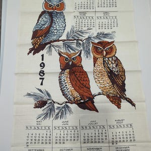 Pode incluir: Uma toalha de calendário vintage com três corujas num galho, datada de 1987. A grelha do calendário mostra os meses em inglês e francês.