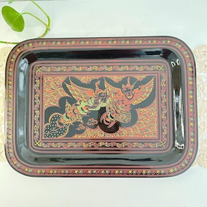Op de afbeelding: Zwarte rechthoekige dienblad met een gedetailleerd, kleurrijk ontwerp met een mythische vogel. De dienblad heeft een rode en gouden rand en een glanzende afwerking. Het centrale ontwerp is in tinten rood, oranje en groen.