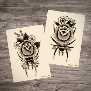 Può includere: Due disegni di flash di tatuaggio in bianco e nero con una rosa e un ragno. La rosa è circondata da foglie e fiori più piccoli. Il ragno ha otto zampe e un corpo rotondo. I disegni sono su uno sfondo crema con il testo "Ashley Love" in basso.