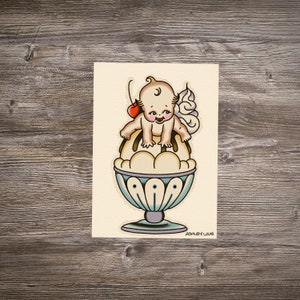 Puede incluir: Una ilustración de estilo vintage de un querubín sentado encima de un gran helado sundae con una cereza en la parte superior. El helado está en un plato de vidrio azul y blanco con un remolino de crema batida en la parte superior. La ilustración es de estilo de dibujos animados y tiene un toque caprichoso.