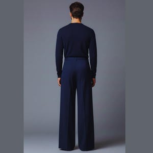 May include: A person wearing a navy blue long-sleeved sweater and matching wide-leg trousers. The outfit is a solid color, with a minimalist design. The model is standing against a gray background.