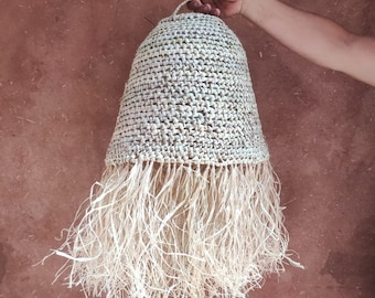 May include: A woven lampshade with a fringe made of natural fibers. The lampshade is beige and has a woven texture. The fringe is long and flowing.