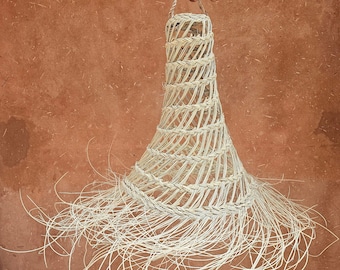 Pode incluir: Uma luminária pendente tecida à mão com um design em forma de sino. A luz é feita de material tecido natural de cor clara, com longas mechas penduradas na parte inferior. A luminária é suspensa por uma alça tecida.