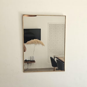 May include: A gold framed mirror reflecting a room with a television, a white decorative wall panel, and two black chairs at a table.