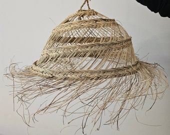 Puede incluir: Una lámpara colgante tejida natural con un borde de flecos. La luz está hecha de materiales naturales y tiene un estilo rústico y bohemio.