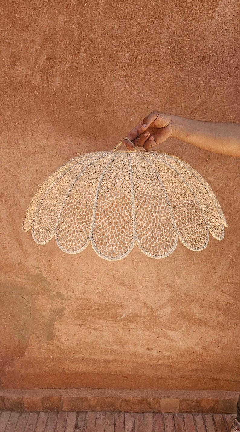 May include: A white crocheted lampshade with a scalloped edge. The lampshade is hanging from a hook.
