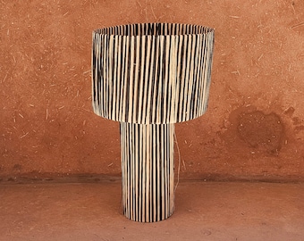 Può includere: Un vaso cilindrico intrecciato nero e naturale con un'ampia parte superiore e una base stretta. Il vaso è realizzato con materiali naturali e presenta un motivo a righe.