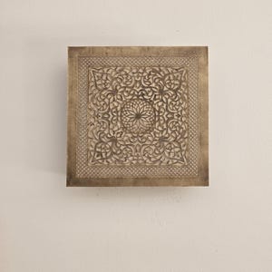 Può includere: Un decoro da parete quadrato in legno intagliato in modo intricato con una finitura marrone. Il design presenta un motivo floreale centrale circondato da motivi floreali più piccoli.