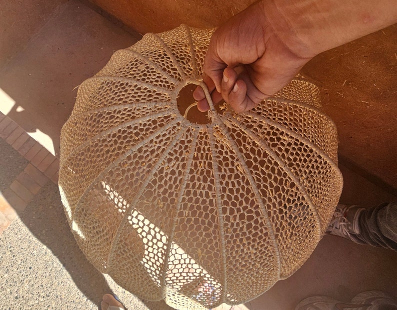 May include: A large, round, woven lampshade made of natural fibres. The lampshade is beige and has a delicate, intricate pattern.