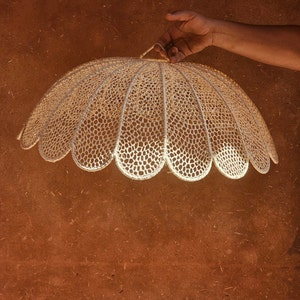 May include: A white crocheted lampshade with a scalloped edge. The lampshade is hanging from a hook.