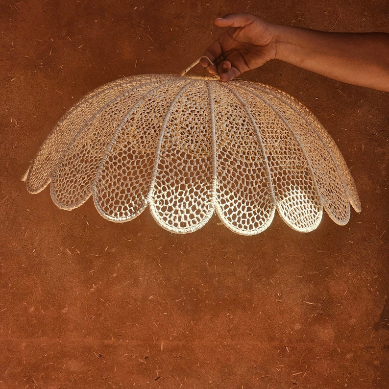 May include: A white crocheted lampshade with a scalloped edge. The lampshade is hanging from a hook.