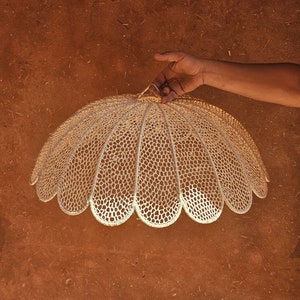 May include: A white crocheted lampshade with a scalloped edge, hanging from a hand.
